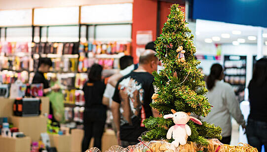Christmas shoppers in a mall, a fake tree is in the foreground